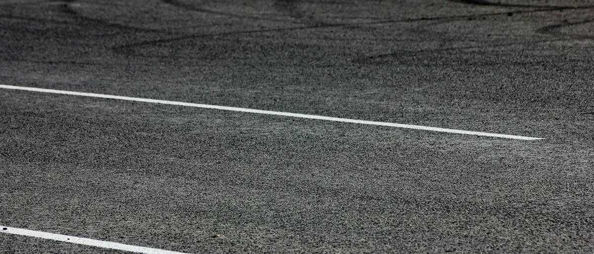 Asphalt surface with painted white lines running across it